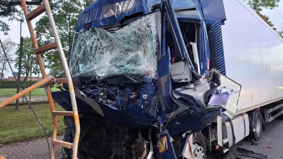 Zniszczona kabina niebieskiego tira z rozbitą szybą, stojącego na poboczu drogi, obok drabina.