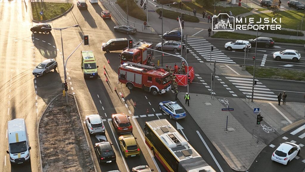 W centrum miasta, zablokowana ulica, na której stoją pojazdy straży pożarnej oraz karetka, a obok widać osoby w mundurach.