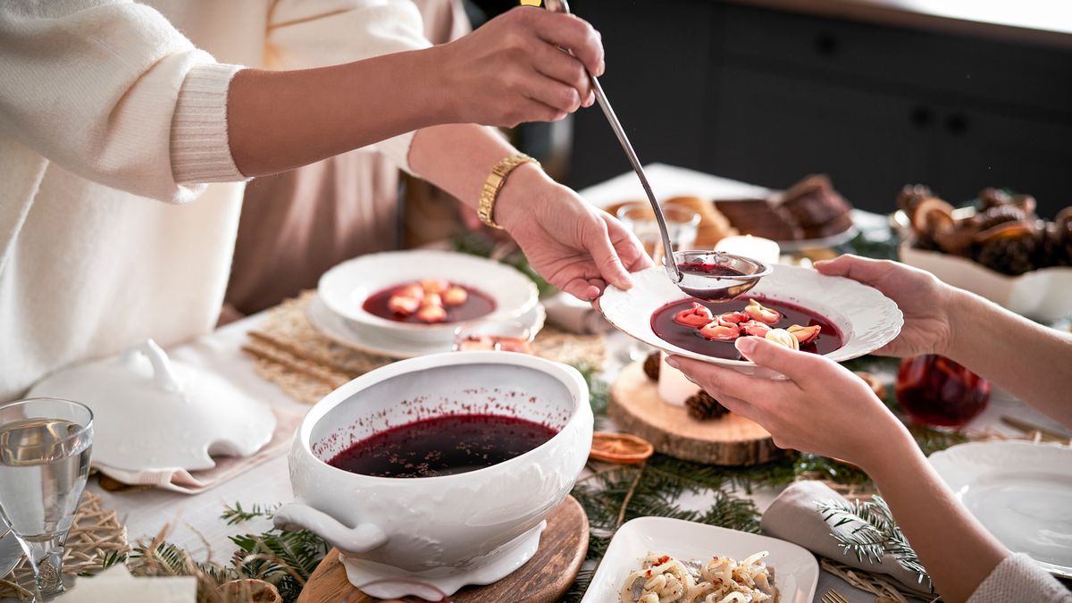 Na zdjęciu stół wigilijny; jedna osoba nalewa drugiej barszcz