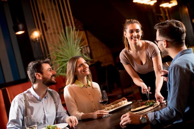 Pretty waiter woman serving group of friends with food in the restaura