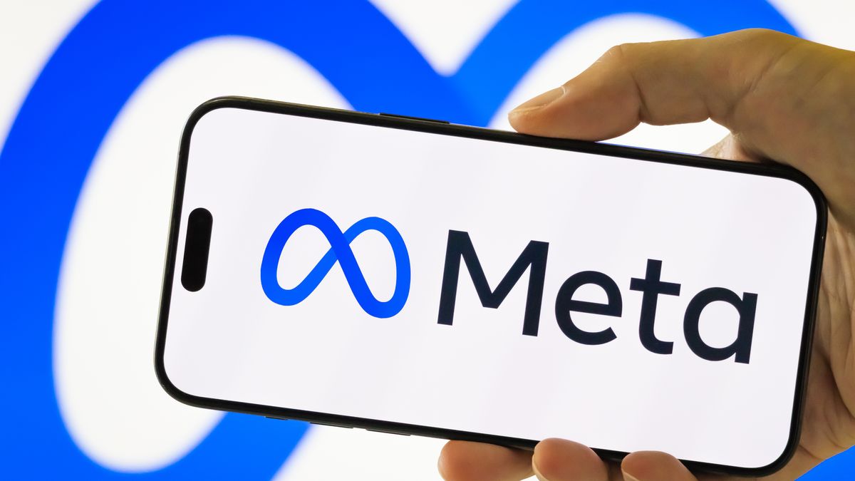 CHONGQING, CHINA - JULY 28: In this photo illustration, a person holds a smartphone displaying the logo of Meta Platforms Inc. (NASDAQ: META), the parent company of Facebook, Instagram, and WhatsApp, with the company's blue infinity loop symbol visible in the background, on July 28, 2025 in Chongqing, China. (Photo illustration by Cheng Xin/Getty Images)