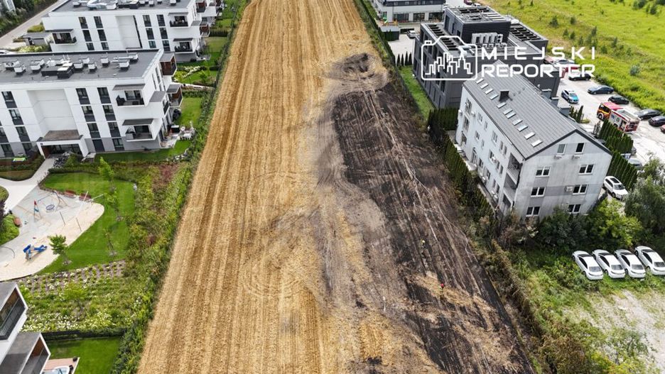 Dwa pracowników w kamizelkach odblaskowych przeszukują teren obok nowoczesnych budynków mieszkalnych.