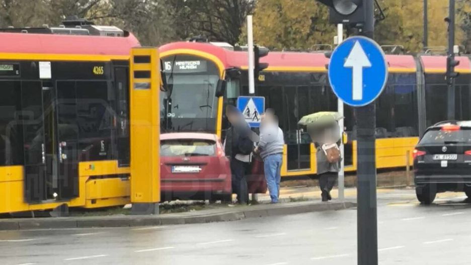 Tramwaj z numerem 16 zatrzymany na przystanku, obok grupka osób rozmawia przy uszkodzonym samochodzie.