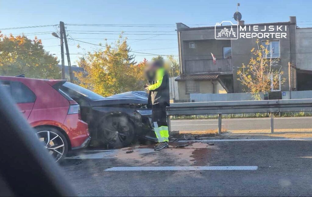Mężczyzna w odblaskowej kamizelce bada uszkodzenia dwóch zderzonych samochodów na drodze krajowej.