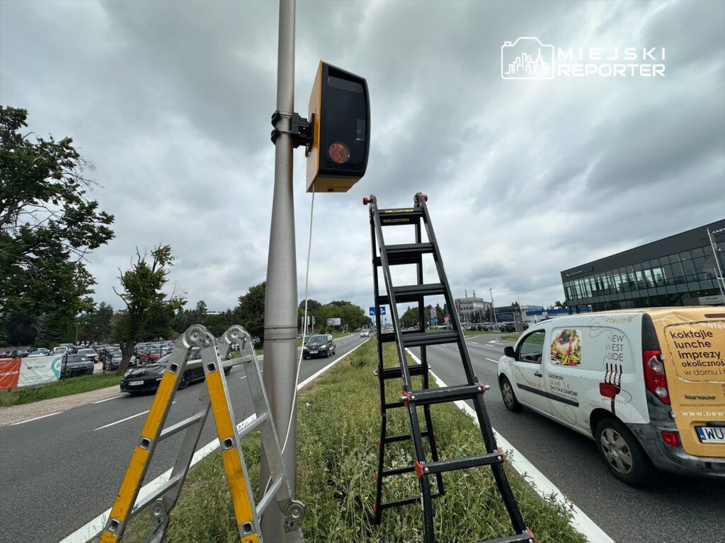 Pracownik wchodzi na drabinę obok nowoczesnego sygnalizatora świetlnego na ruchliwej drodze.
