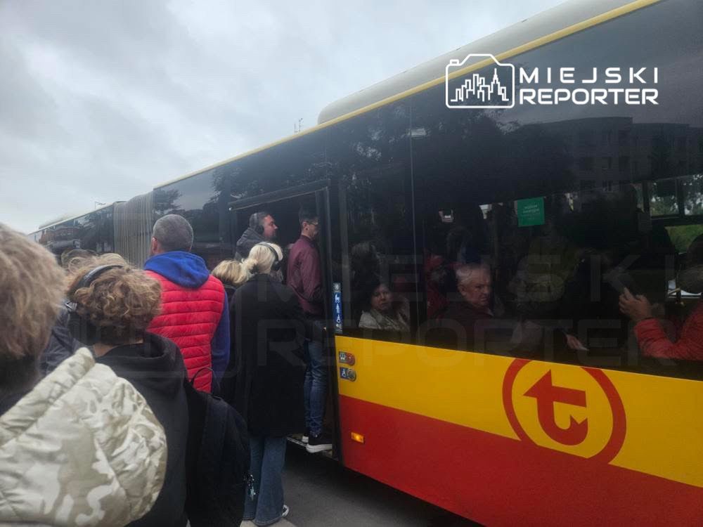 Grupa osób czeka w kolejce, aby wsiąść do autobusu miejskiego z żółto-czarną kolorystyką.