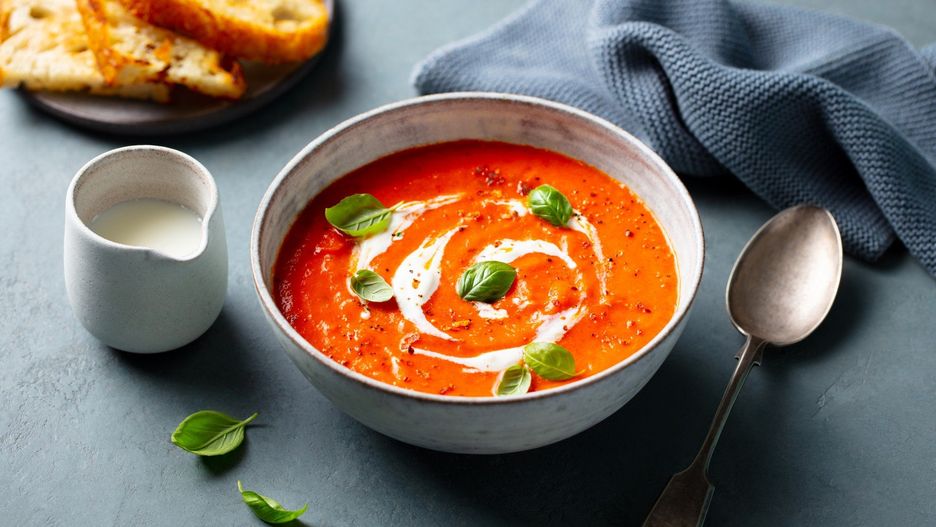 Tomato soup with cream and basil leaf in a white bowl on grey background. Close up.