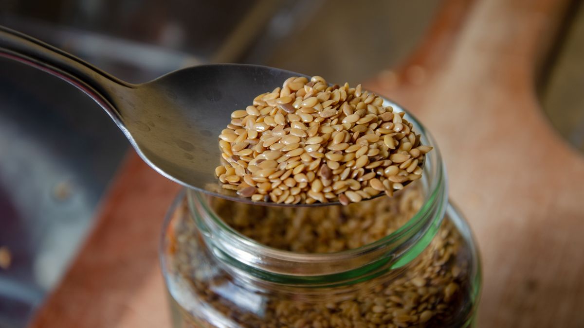 spoon over a glass jar full of linseed on wooden cutting boardclose up on a spoon over a glass jar full of linseed on wooden cutting boardGrazieGranatasugar, golden linseed