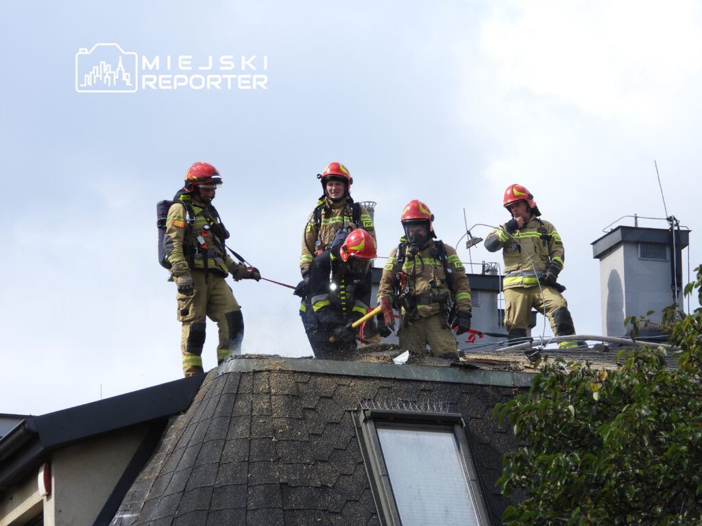 Grupa strażaków w hełmach i mundurach pracuje na dachu budynku, usuwając niebezpieczne materiały.