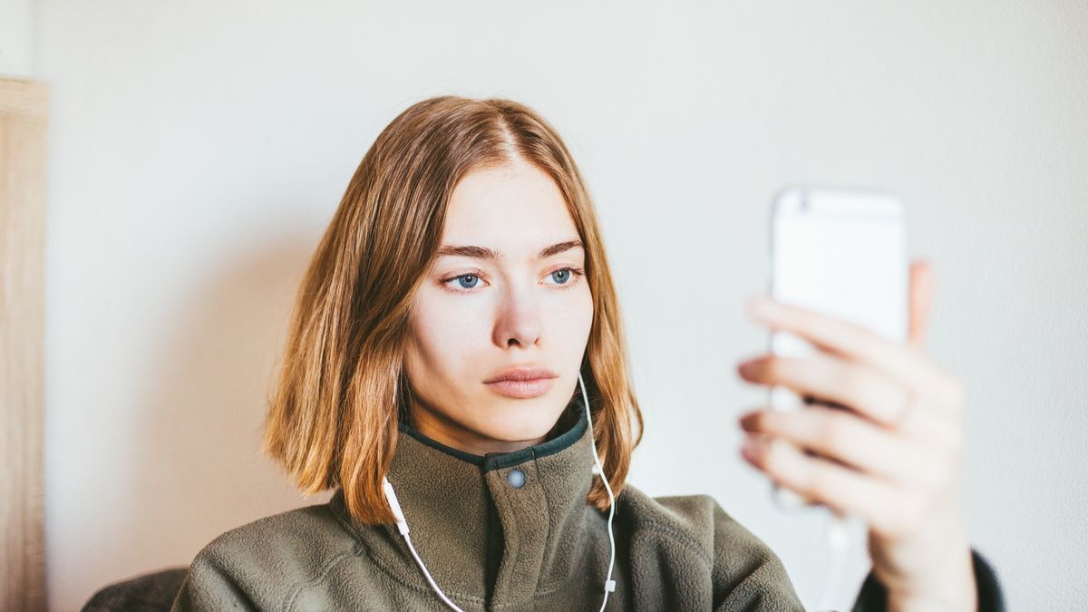 Młoda kobieta ze słuchawkami w uszach jest wpatrzona w telefon
