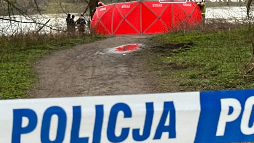 Funkcjonariusze policji zabezpieczają teren przy rzece, gdzie znajdują się zwłoki, otoczeni przez czerwony namiot.