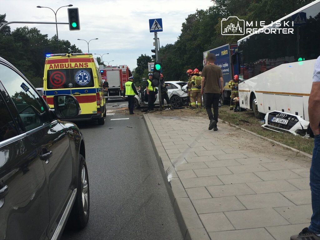 Wielu ratowników i strażaków udziela pomocy poszkodowanym po wypadku drogowym obok przystanku autobusowego.