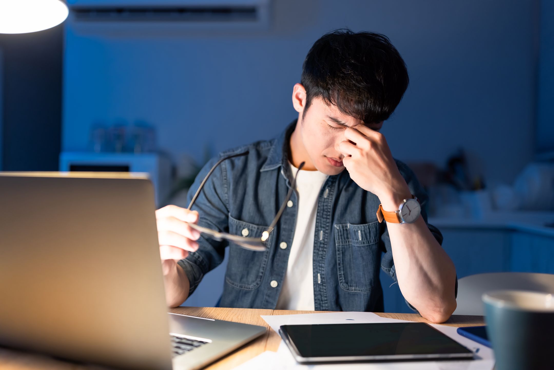 Tired overworked asian male feeling eyes strain after using computer while working at home