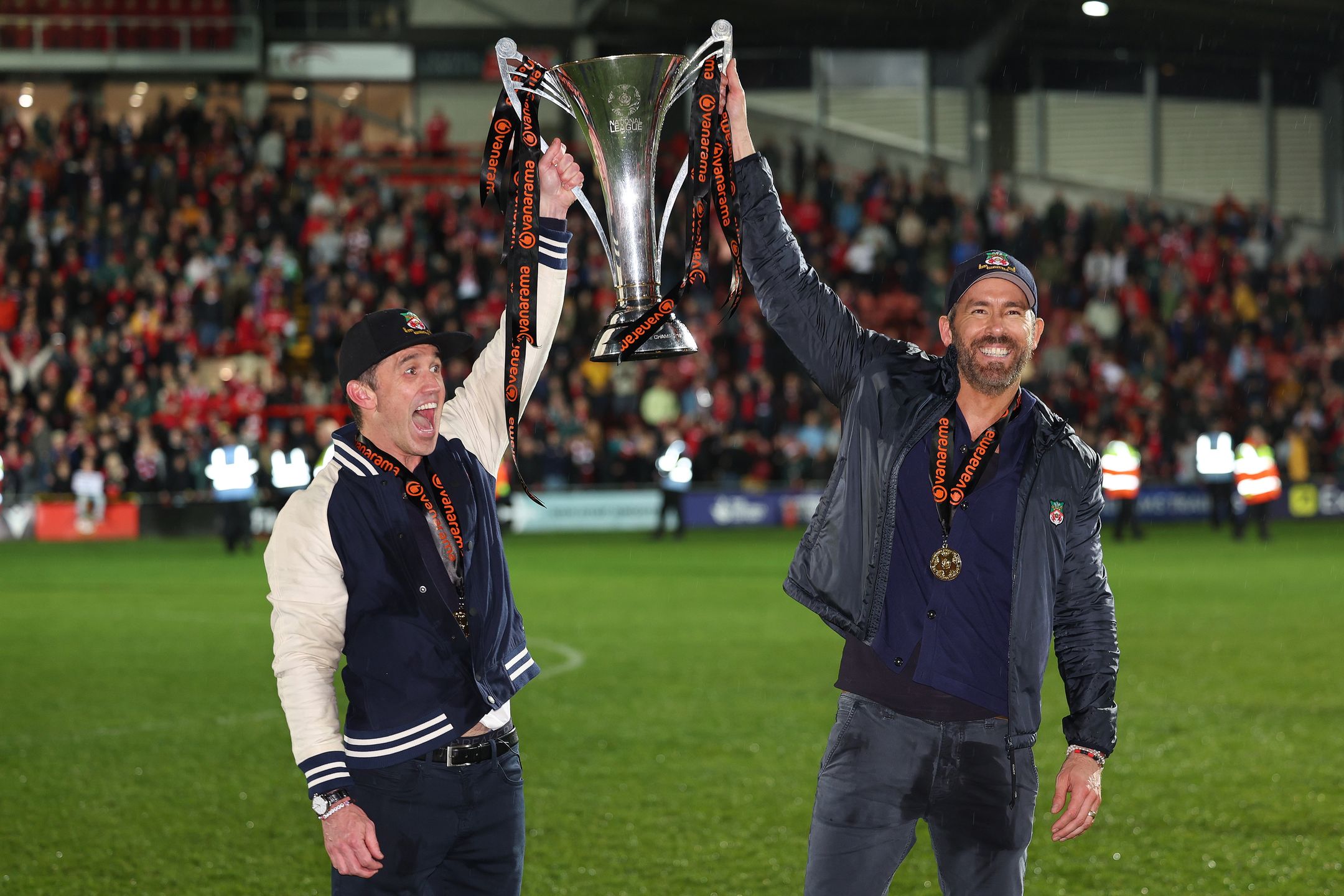 WREXHAM, WALES - APRIL 22: Wrexham owners Rob McElhenney and Ryan Reynolds hold the Vanarama National League Trophy as Wrexham celebrate promotion back to the English Football League during the Vanarama National League match between Wrexham and Boreham Wood at Racecourse Ground on April 22, 2023 in Wrexham, Wales. (Photo by Matthew Ashton - AMA/Getty Images)