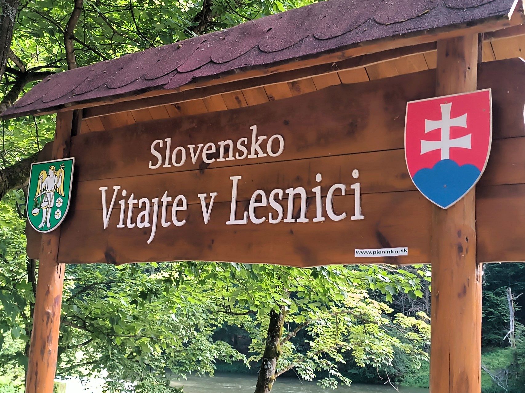 Drewniana tablica z napisem Slovensko, Vitajte v Lesnici i słowackim godłem przy drodze w lesie