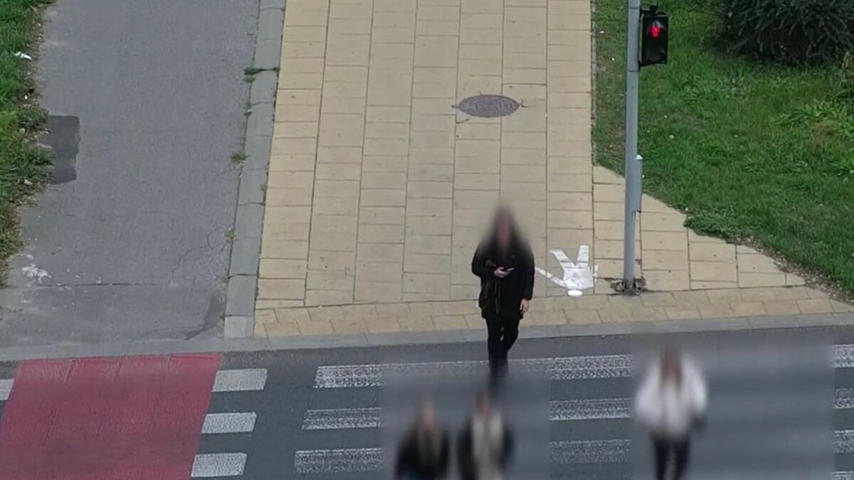 Pieszy z telefonem w ręku przechodzi przez przejście na czerwonym świetle