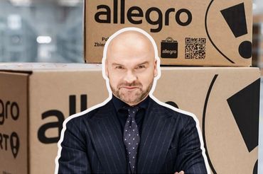 Rafał Brzoska na tle paczek z Allegro, fot. mat. prasowe