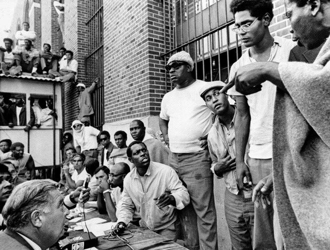 Komisarz Russell Oswald (siedzi, lewy dolny róg) podczas negocjacji z przywódcami więźniów wśród
których są Frank "Big Black” Smith (w okularach przeciwsłonecznych) oraz L.D. Barkley (drugi od prawej).
(Dzięki uprzejmości "New York Timesa”)
