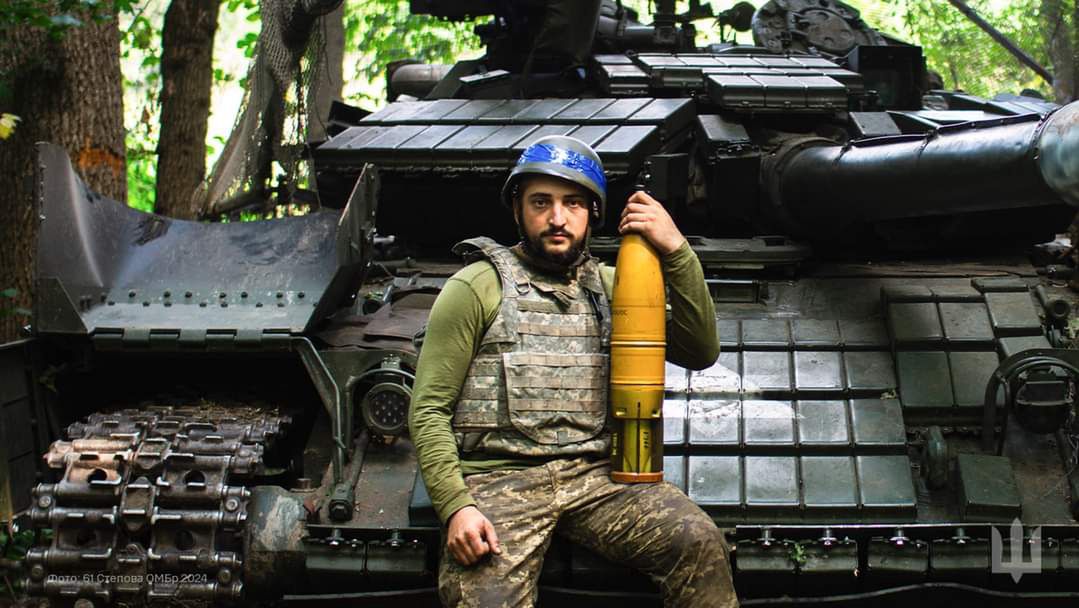 A soldier standing in front of a T-64BW tank holding a missile from India.