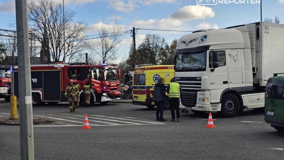 Strażacy w mundurach rozmawiają przy wozie strażackim obok ciężarówki i karetki na skrzyżowaniu.