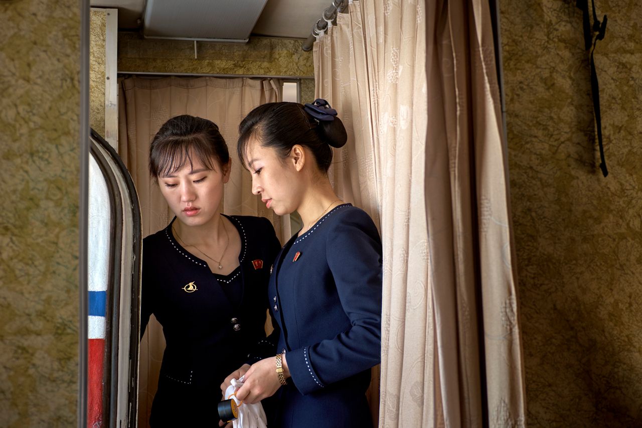 Starsza stewardessa tłumaczy jak otwierać drzwi.