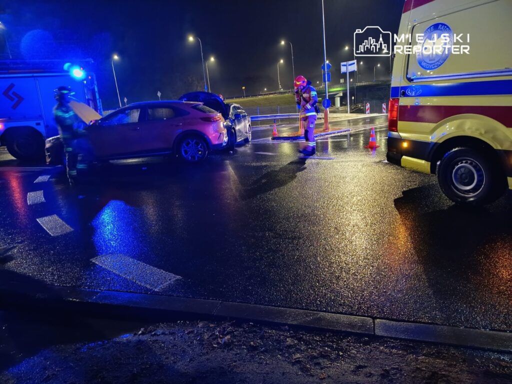Ratownicy medyczni i strażacy pracują przy zderzeniu dwóch samochodów na mokrej jezdni w nocy.