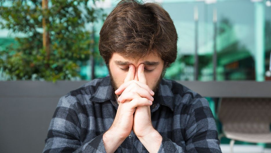 Thoughtful man touching nose bridge and thinking in street cafe