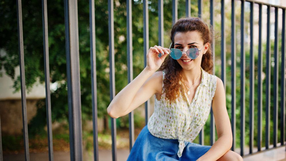 Do rozkloszowanej jeansowej spódnicy pasuje bluzka w kwiatki oraz stylowe okulary