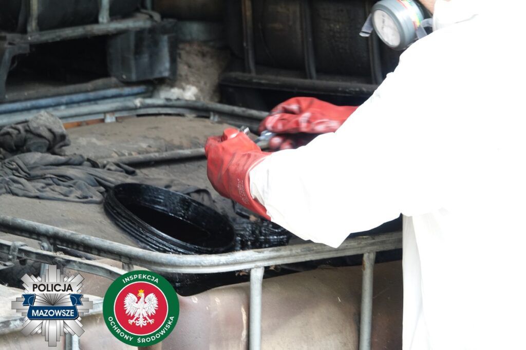 Mężczyzna w rękawicach gumowych przeprowadza kontrolę substancji w pojemniku w zakładzie przemysłowym.