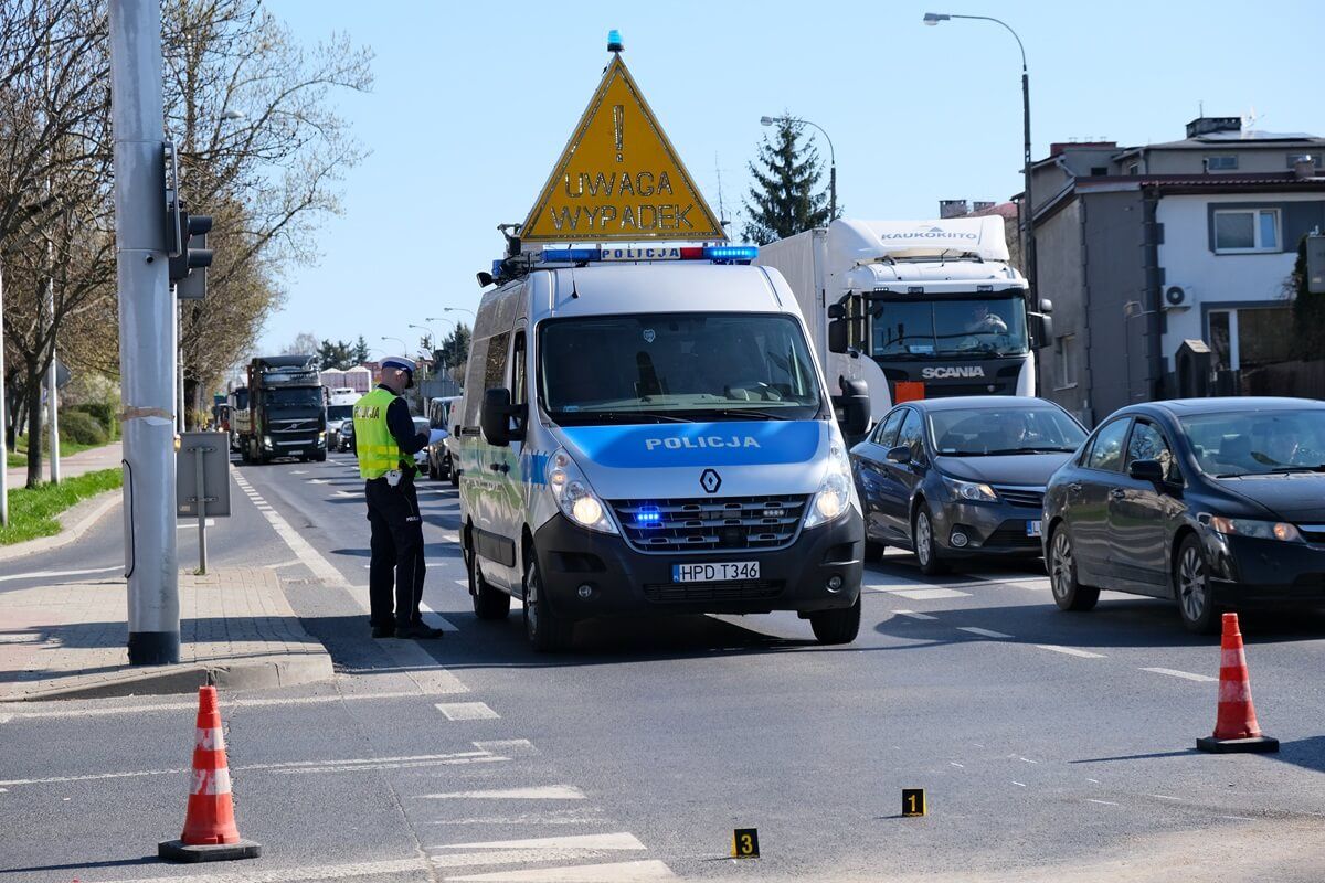 Policjanci pracujący na miejscu wypadku - radiowóz z tablicą "Uwaga wypadek"