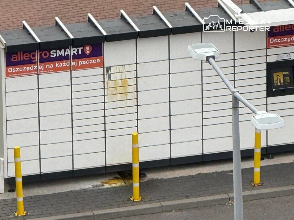 Pusty kiosk paczkowy z reklamą „allegro SMART!” oraz napisem „Oszczędzaj na każdej paczce” na białej ścianie.