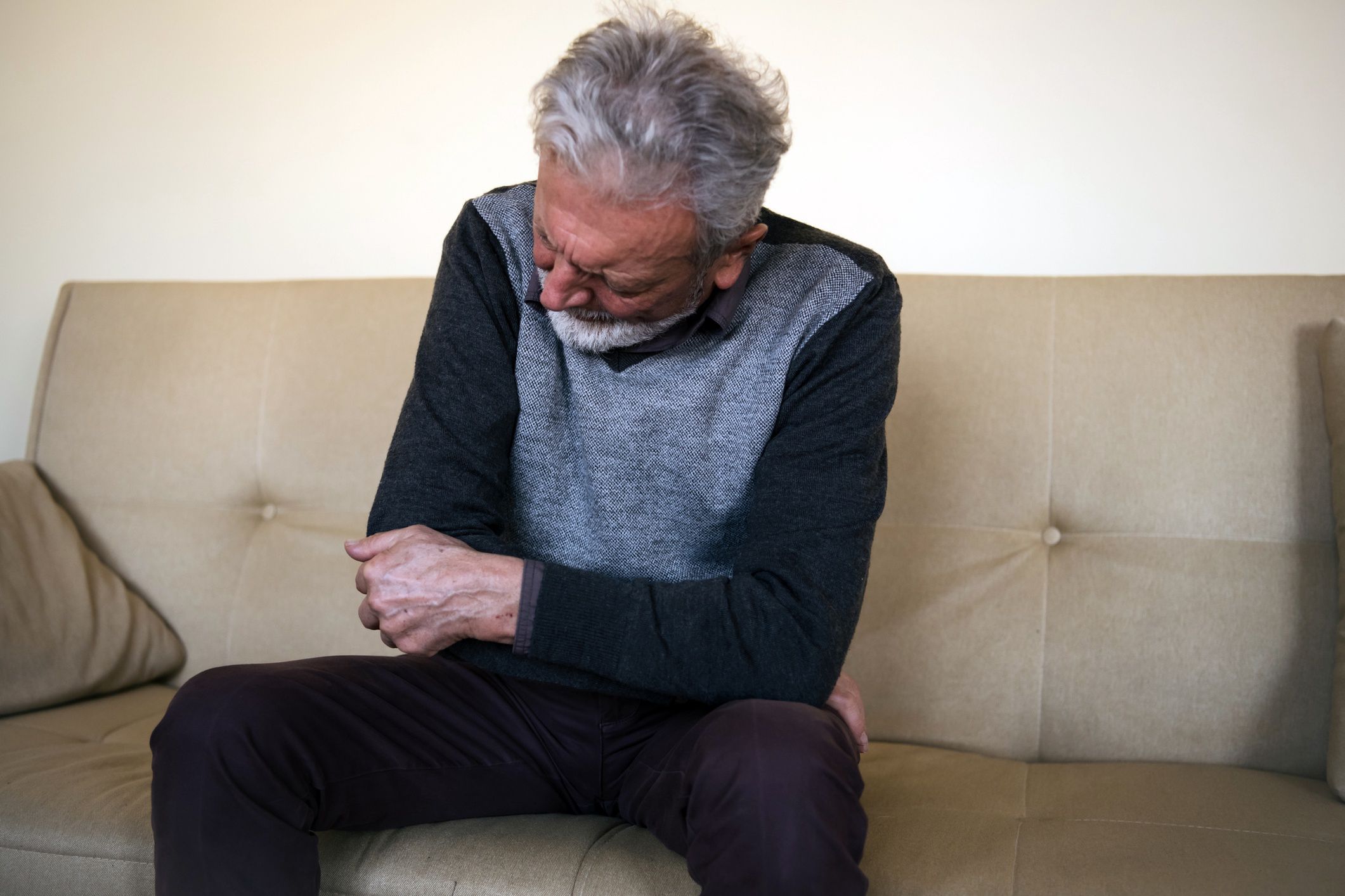 Senior man with a pain in the elbowPhoto of a senior man feeling insufferable pain in the elbow. An elderly man is lying on the sofa at home and holding his elbow due to hard pain.RealPeopleGroup