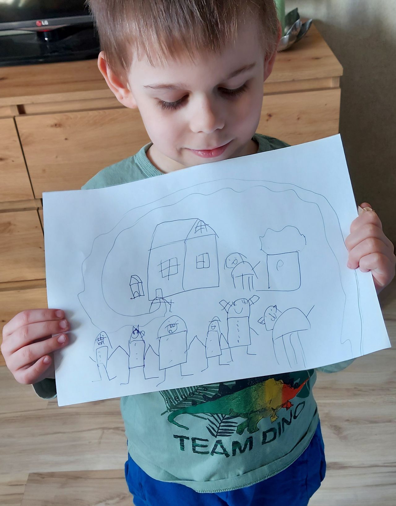 Julian pokazuje narysowany przez siebie dom. Obrazek to prezent dla taty 
