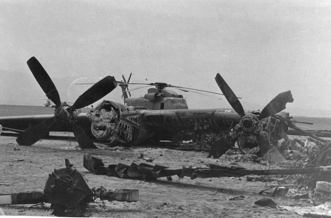 Desert One - fragment spalonego samolotu i stojący w oddali smigłowiec