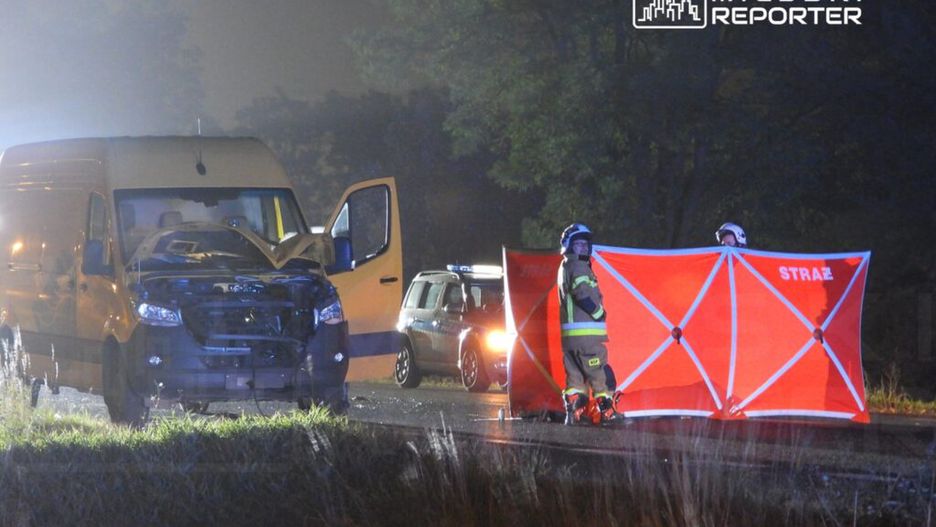 Na drodze stoi uszkodzony furgon, a obok niego strażacy z czerwonym parawanem, zabezpieczający miejsce zdarzenia.