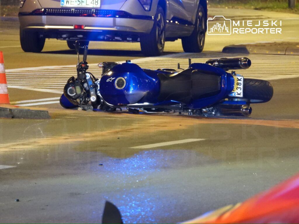 Nieprzewidziana sytuacja na drodze: przewrócony niebieski motocykl leży na jezdni obok pojazdu osobowego.
