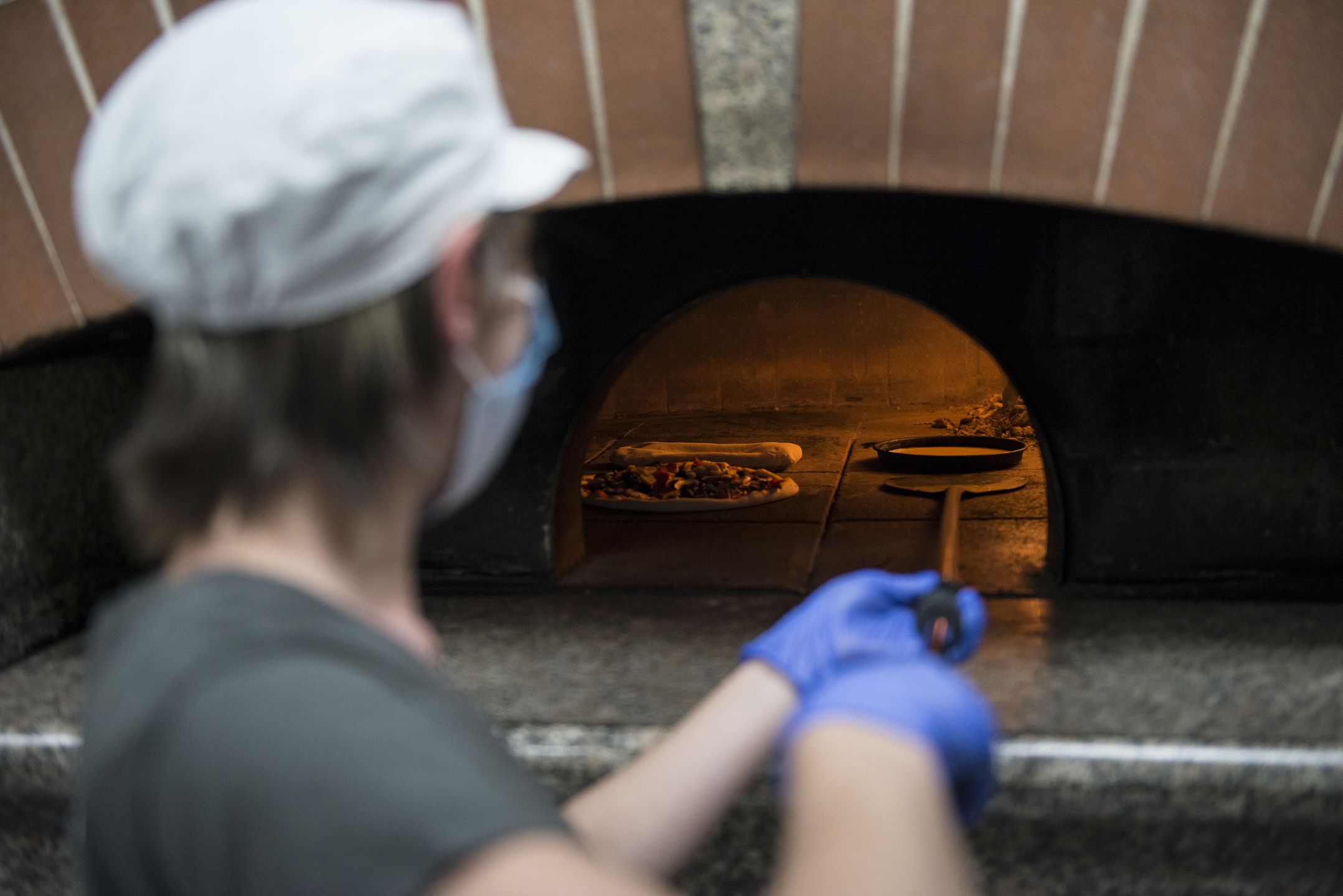 TURIN, ITALY - MAY 01: The pizza maker wearing protective face mask cooking takeaway pizza in the oven inside a pizza take-away on May 01, 2020 in Turin, Italy. Italy will remain on lockdown to stem the transmission of the Coronavirus (Covid-19), slowly easing restrictions. (Photo by Stefano Guidi/Getty Images)
