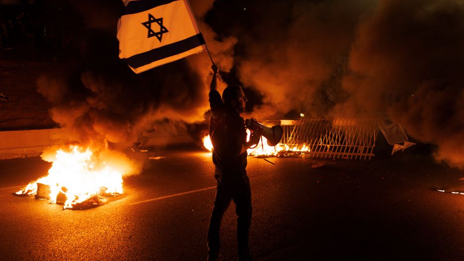 A demonstrator waves an Israeli national flag at a road block on the Ayalon Highway during a protest against prime minister Benjamin Netanyahus coalition government and proposed judicial reforms in Tel Aviv, Israel, on Sunday, March 26, 2023. Thousands of protesters took to the streets in Israel overnight, including around  Netanyahus home, after the prime minister fired his defense chief over a dramatic speech criticizing a contentious plan to reduce the power of the Supreme Court. Photographer: Kobi Wolf/Bloomberg via Getty Images