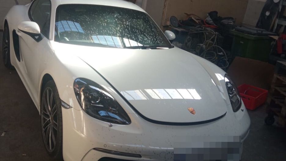 Biały sportowy samochód marki Porsche zaparkowany w warsztacie, otoczony narzędziami i częściami.
