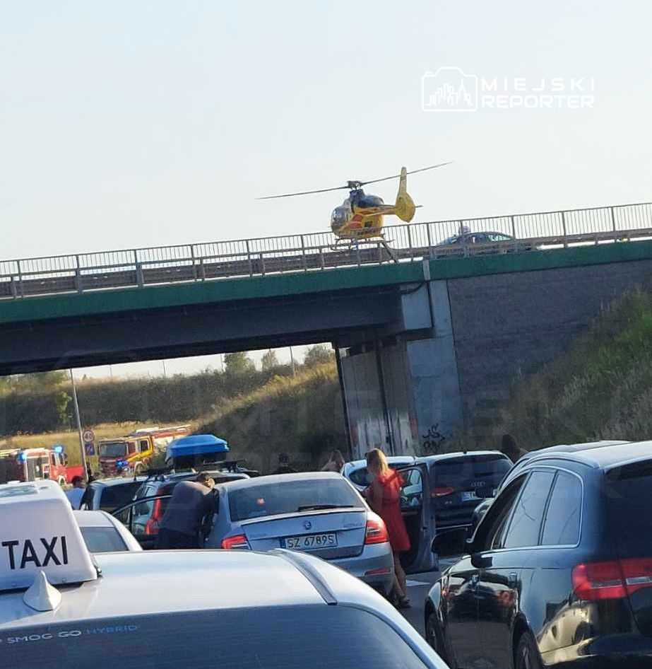 Helikopter ratunkowy ląduje na moście, podczas gdy zablokowane samochody stoją w korku pod nim.