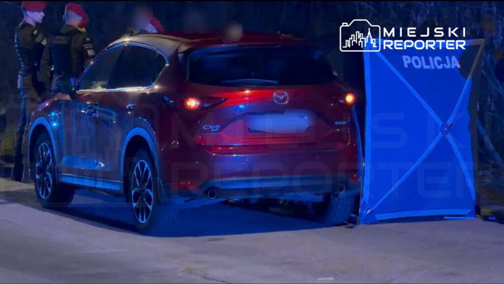 Czerwony samochód marki Mazda CX-5 zaparkowany obok niebieskiego namiotu z napisem "POLICJA", w tle policjanci.