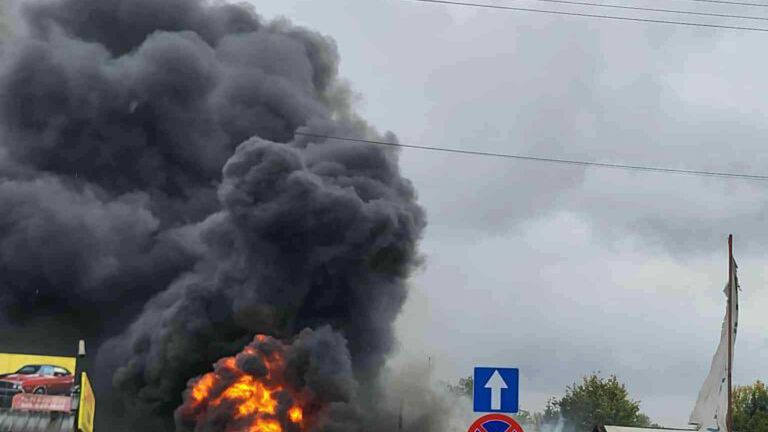 Pożar w budynku, z którego wydobywa się czarny dym i płomienie, w otoczeniu zaparkowanych samochodów.