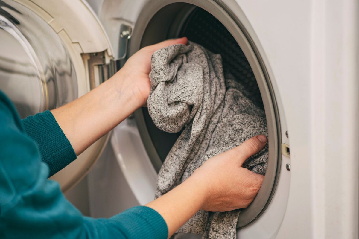 The woman puts the sweater into the washing machine.