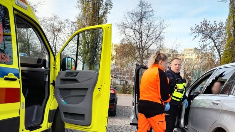 Ratowniczka medyczna i strażnik miejski między karetką a samochodem.