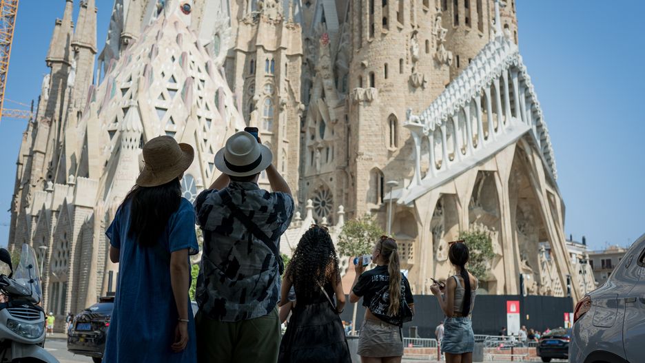 BARCELONA, SPAIN - 2024/08/21: Tourists take pictures of the Sagrada Familia church in the city center. With more than 18 million tourists expected to visit Barcelona in 2024, the city is struggling to find a balance between the economic benefits of tourism during the tourist season, and the need to keep the city liveable for local residents, who are showing hostility towards the mass tourism and the exploitation of the city by the tourism industry. (Photo by Davide Bonaldo/SOPA Images/LightRocket via Getty Images)