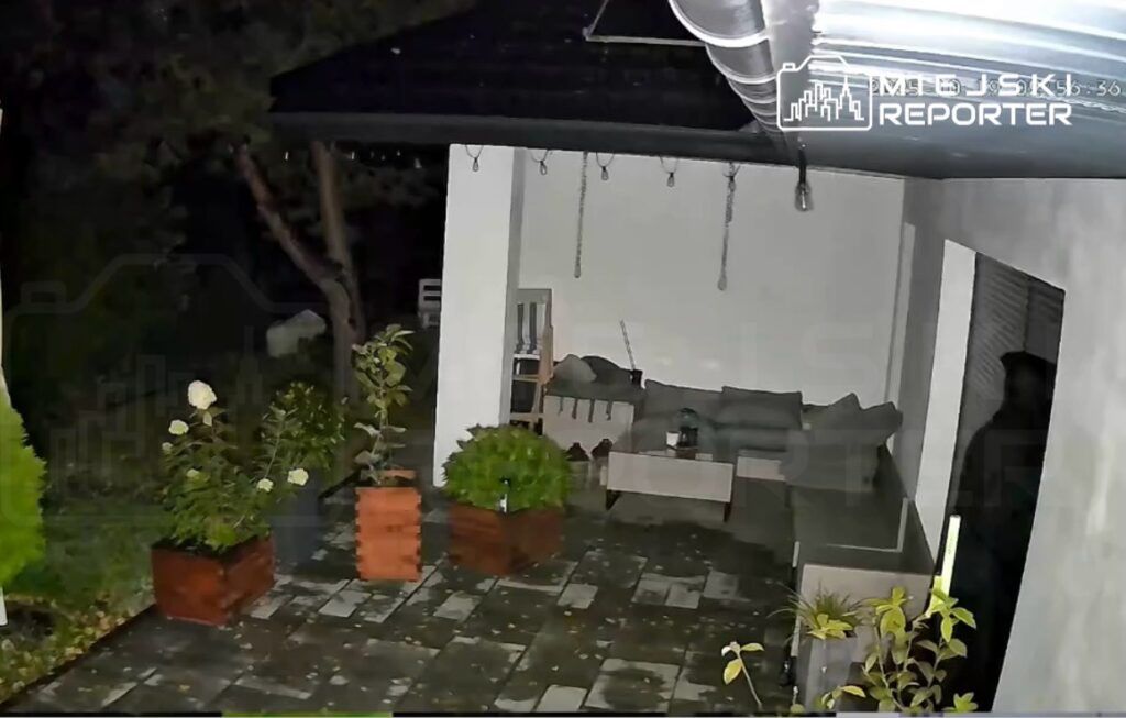 Oświetlony taras z meblami ogrodowymi, donicami z roślinami i płytkami na podłodze, otoczony ciemnym ogrodem.