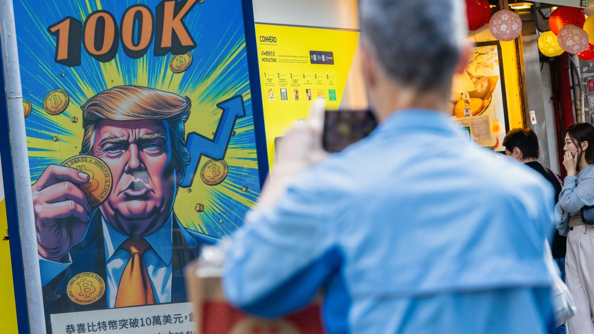 A cartoon image of US President-elect Donald Trump holding a Bitcoin token to mark the cryptocurrency reaching over $100,000 displayed at a Coinhero store in Hong Kong, China, on in Hong Kong, China, on Thursday, Dec. 5, 2024. Trump's pick of a crypto proponent to be the next head of the US securities regulator lifted Bitcoin to $100,000 for the first time as traders warmed to the prospect of relaxed regulations. Photographer: Paul Yeung/Bloomberg via Getty Images