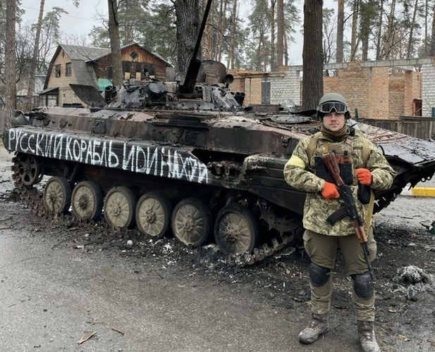 Maksim Lewczenko na tle zniszczonego rosyjskiego czołgu na samym początku wojny w Ukrainie