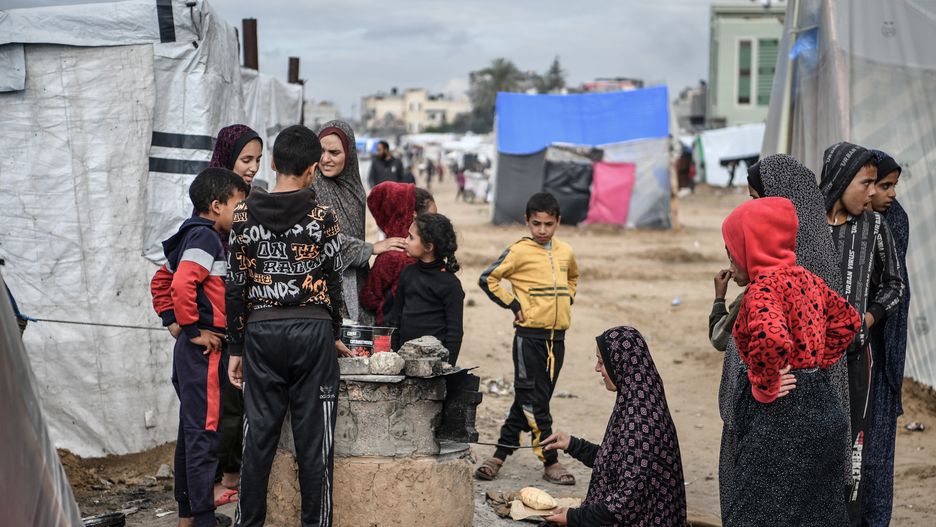 RAFAH, GAZA - FEBRUARY 18: A Palestinian woman, who took refuge in the city of Rafah, cooks the meal on wood fire in front of the makeshift tents where Palestinian families taking shelter as Israel's air, land and sea attacks continue on the Gaza Strip on February 18, 2024 in Rafah, Gaza. Palestinians who escaped from the bombardment of the Israeli army and took shelter in the city of Rafah are trying to continue their daily life in makeshift tents with limited resources and under difficult conditions. (Photo by Abed Zagout/Anadolu via Getty Images)