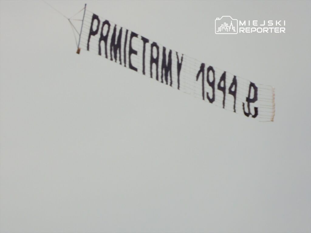 Transparent z napisem "PAMIĘTAMY 1944" zawieszony w powietrzu na tle szarego nieba.